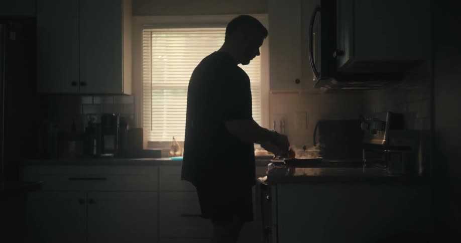 A silhouette of a man in a kitchen cooking something