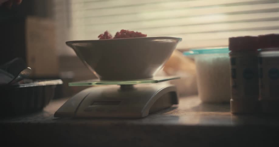 A person preparing food and placing it in a bowl on a scale before picking it up