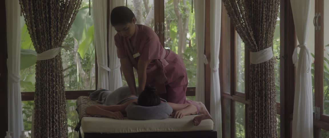 A masseuse leans forward as she pressing down on a womans back