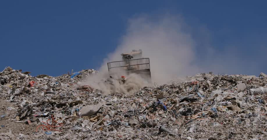 A bulldozer moving through garbage covered land on a bright sunny day