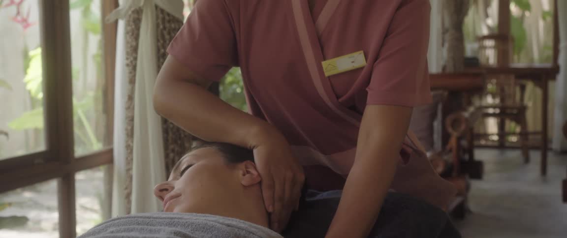 Masseuse carefully stretches neck of woman lying on table in spa