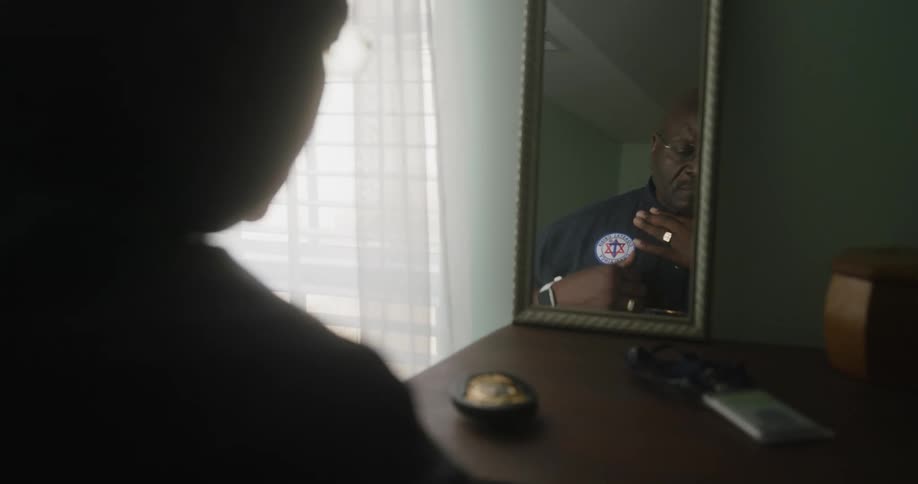 Public official adjusting his polo shirt in front of the mirror and then picking up his badge