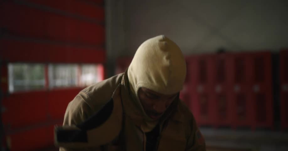 A fireman putting his jacket and equipment on in the middle of a fire station