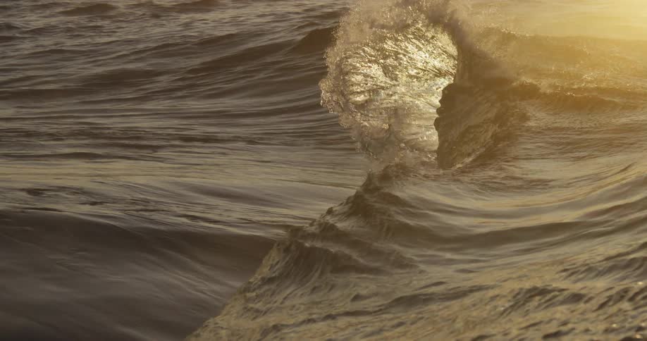 Ocean waves crashing onto the water surface as the sun reflects off the water