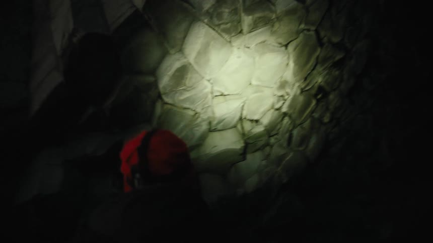 Man in a beanie with a headlamp walking and inspecting a rocky wall