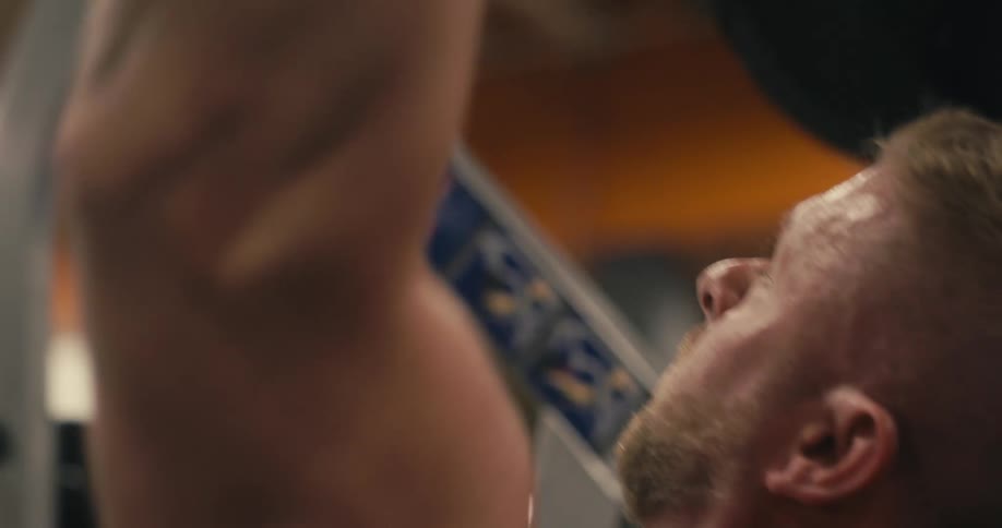 A blond man lifting weights and sweating with the effort