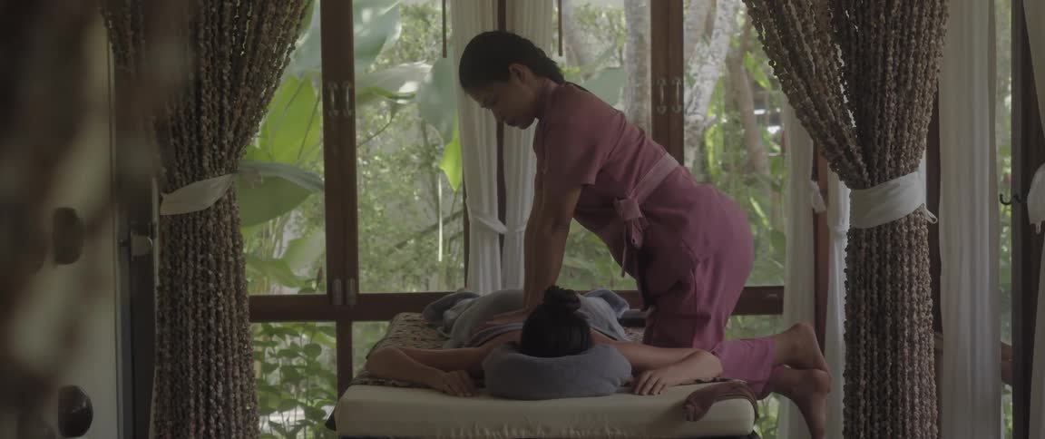 Masseuse kneels while massaging back of woman lying on table