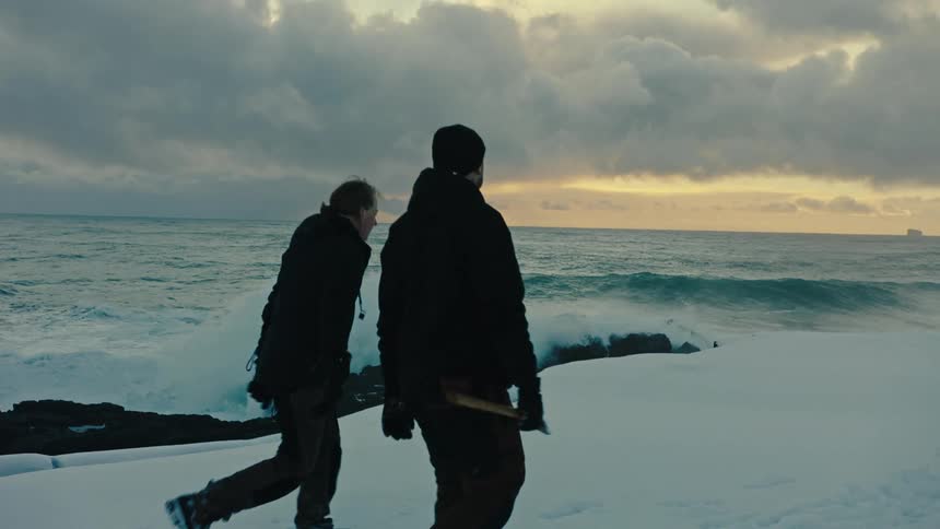 Two men walking along an icy shoreline next to a sea