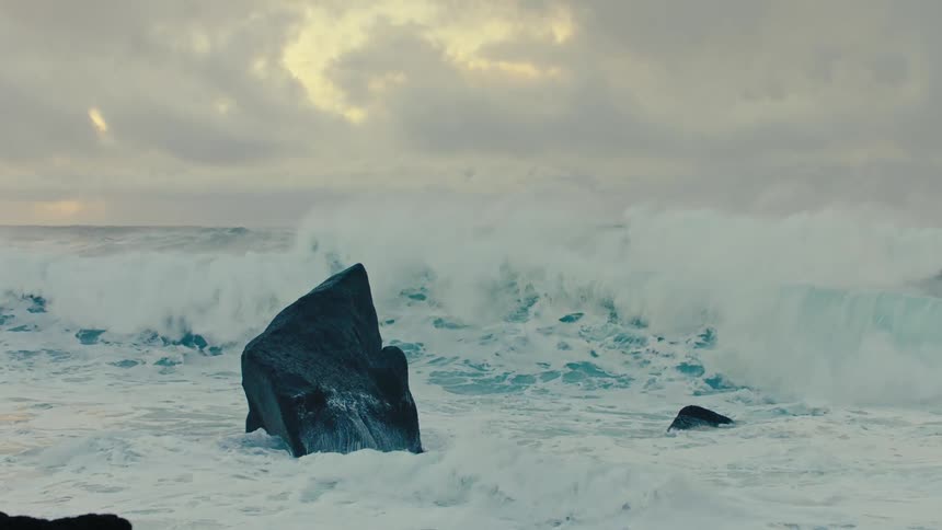 Ocean waves crashing against rocks on a coast in the middle of the day with clouds in the sky