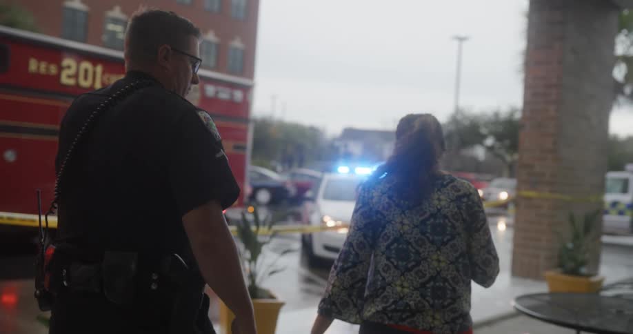 Police officer walking alongside a woman with various police vehicles an ambulance and a fire truck in the background