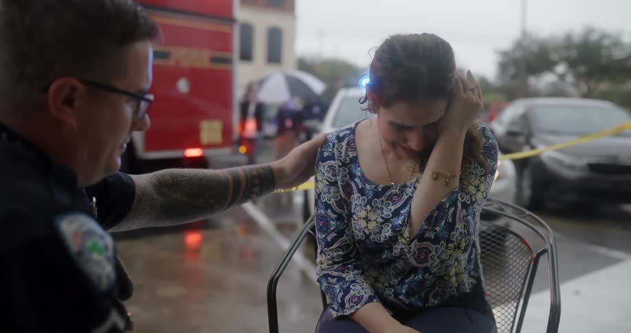Police officer comforting a crying woman with police cars and a fire truck in the background