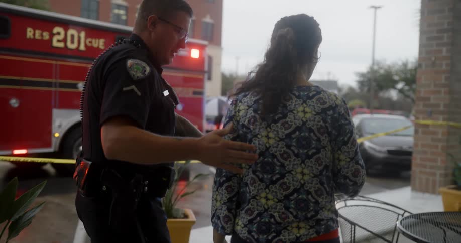 Police officer walking with a frightenedlooking woman with vehicles and a fire truck in the background