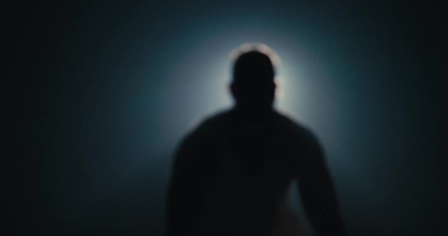 Silhouette of a strong muscular man lifting weights in front of a spotlight