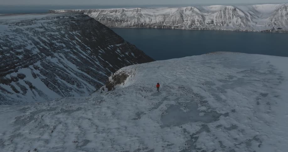Man hiking in icecovered mountains with a lake in the background