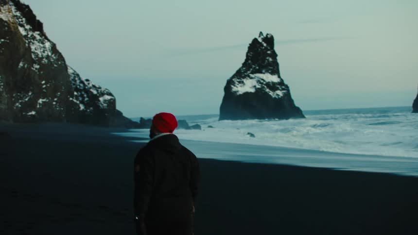A man walking on the beach with rocky mountains with snow on the peak