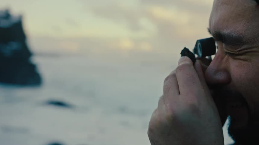 Man standing on beach during winter examines rough stone with a jewelers loop
