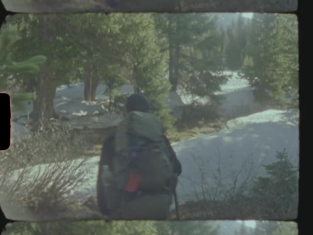 Man with a hiking backpack walking in an open forest with snowcovered ground