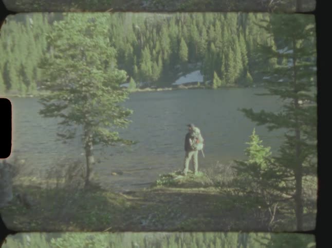 A man with a backpack standing near a river on a sunny day