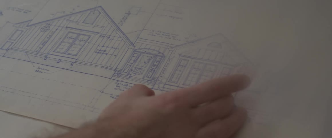 Human hands pointing to a drawing of a blueprint for a house on paper