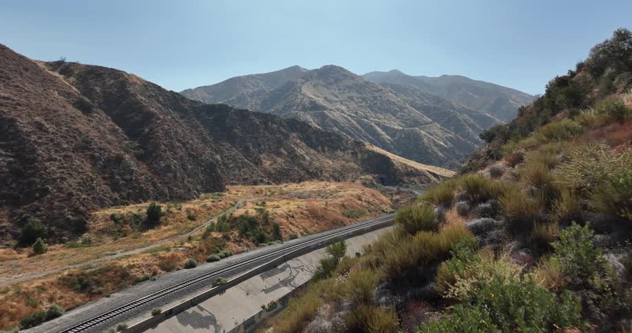 View of train tracks in the midst of nature surrounded by a chain of mountains