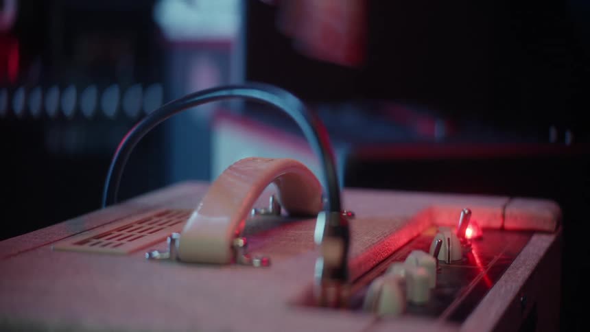 Human hands plugging a cable into an amplifier and pressing a button that turns on and lights up a red led