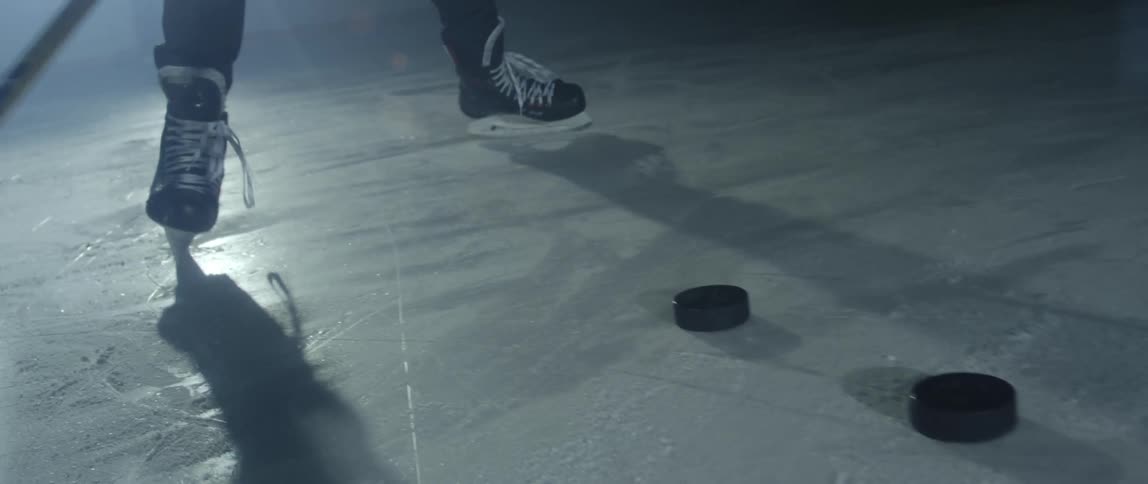 Man playing hockey on ice indoors hitting a row of pucks with the stick
