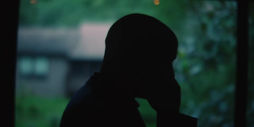 Man silhouetted against window talks on phone