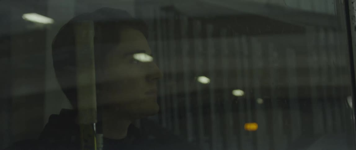Man stands staring through the glass at a hockey rink as ceiling lights come on