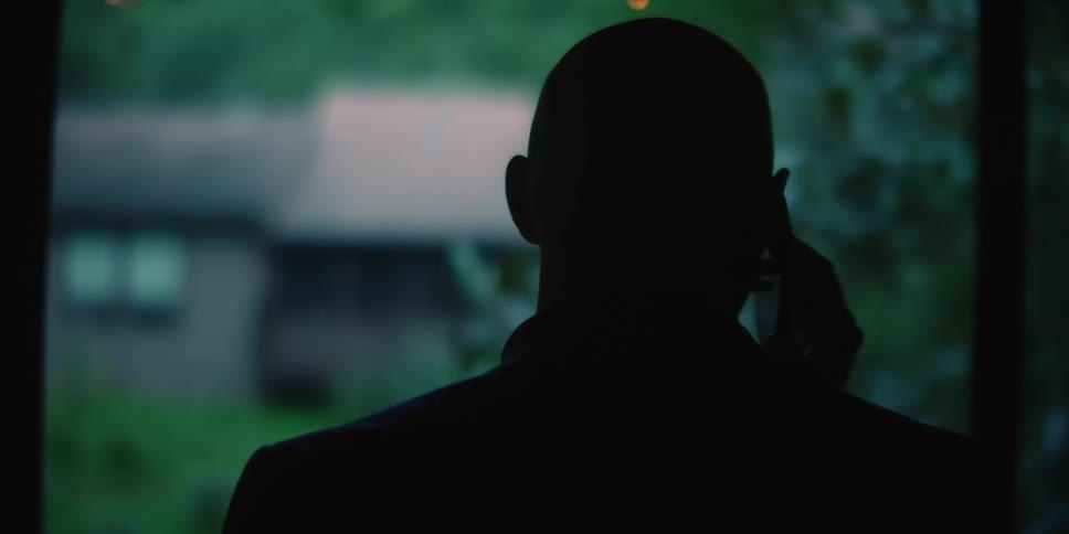 The backside of a man talking on his cellphone while standing in front of a window