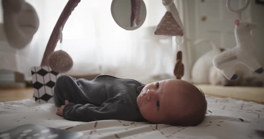 Baby lays on floor below a mobile