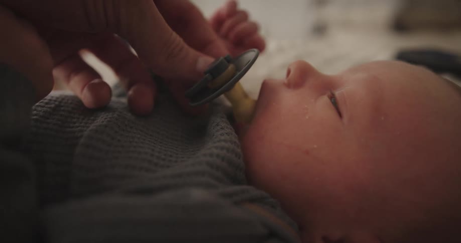 A baby is lying down as their mother puts a pacifier in their mouth