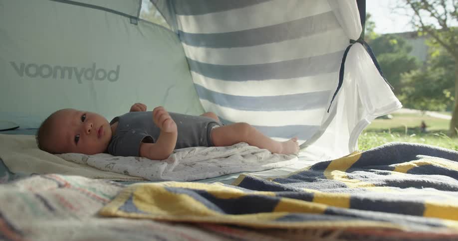 A baby lying on a blanket inside a sun shelter on a sunny day in the park