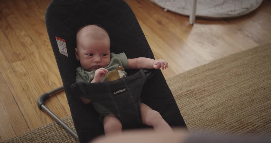 An infant sits in a chair moving its arms and legs in a room