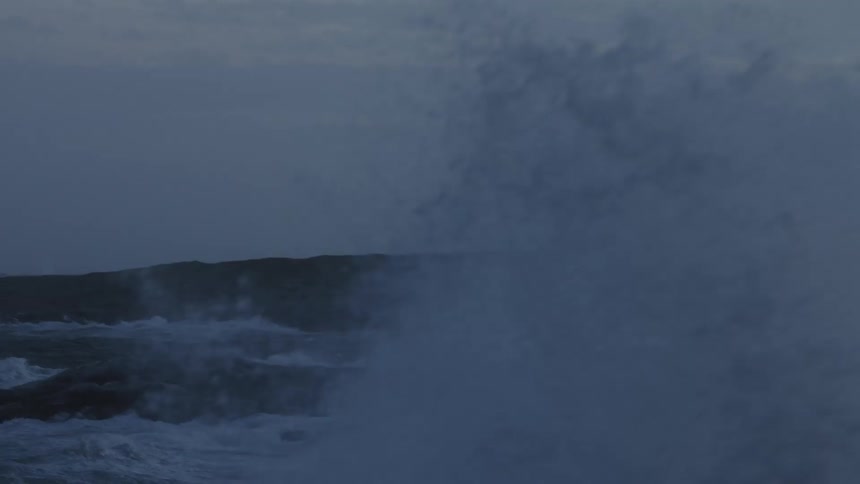 View of the sea with strong waves crashing on rocky cliffs and in the background a tower with a light