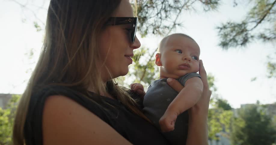 Mother holds her newborn baby in the backyard at morning