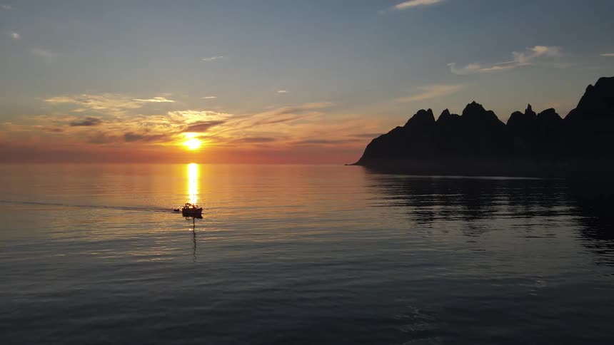 Sail boat moving over waters next to a promontory during dusk or dawn