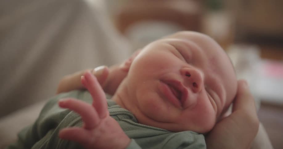 Mother holds sleepy baby in her hands and strokes its head