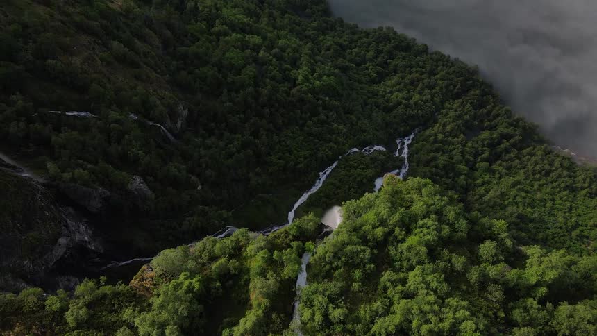 Mountain covered in a forest above the cloud level with a waterfall in free fall