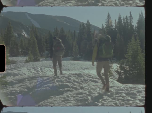 Two people hike across snowy forest terrain wearing backpacks