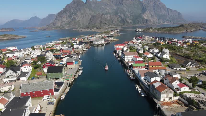 Aerial of a boat sailing through a river between a village with houses on either side