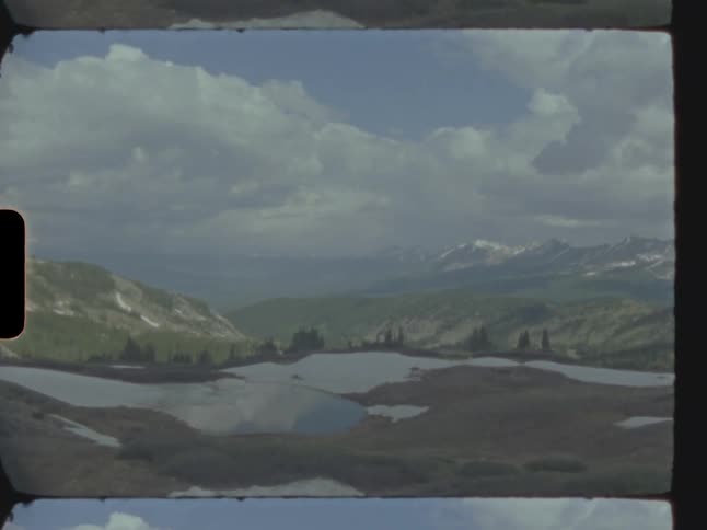A natural landscape with mountains surrounding snow in a valley with a small lake