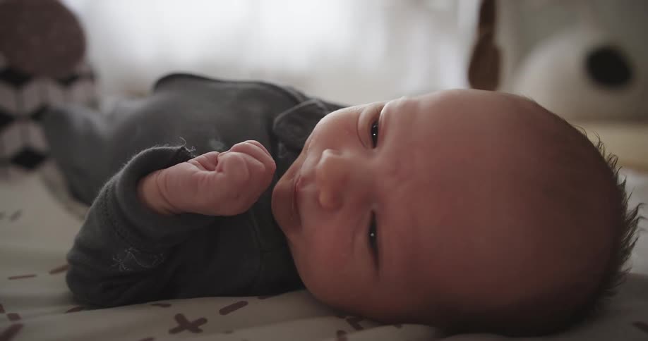 Newborn baby lying in bed moving his arms and legs and looking around indoors during day time