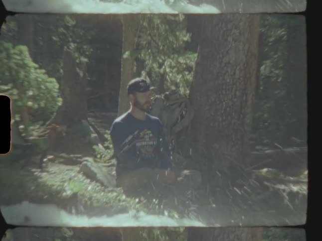 Man sits in forest next to river rapids