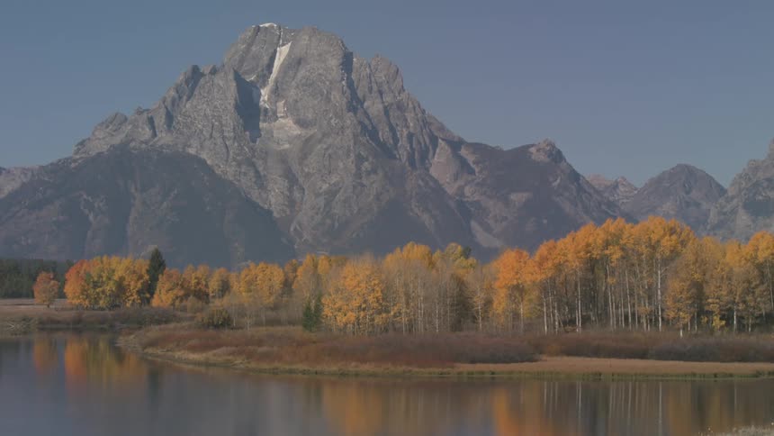 Natural area with yellowing trees by a lake and in the background mountains and cliffs