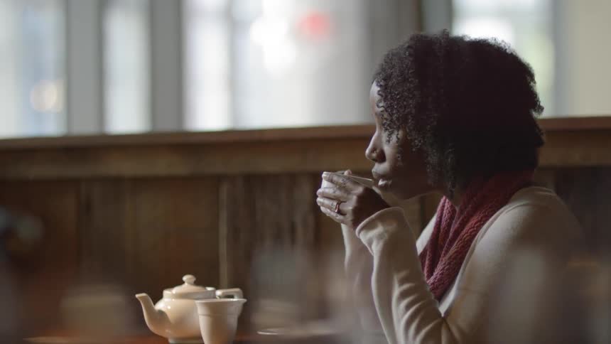 Woman stirring her warm drink while sitting at a cafe table and then taking a sip