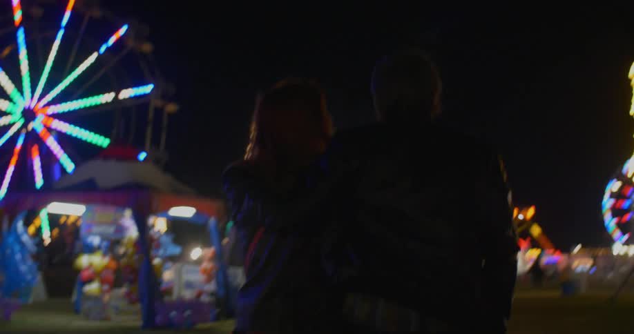 Man and woman walk through fairgrounds at night