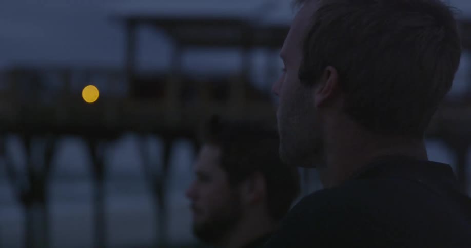 Men talking on the beach near a pier at dusk