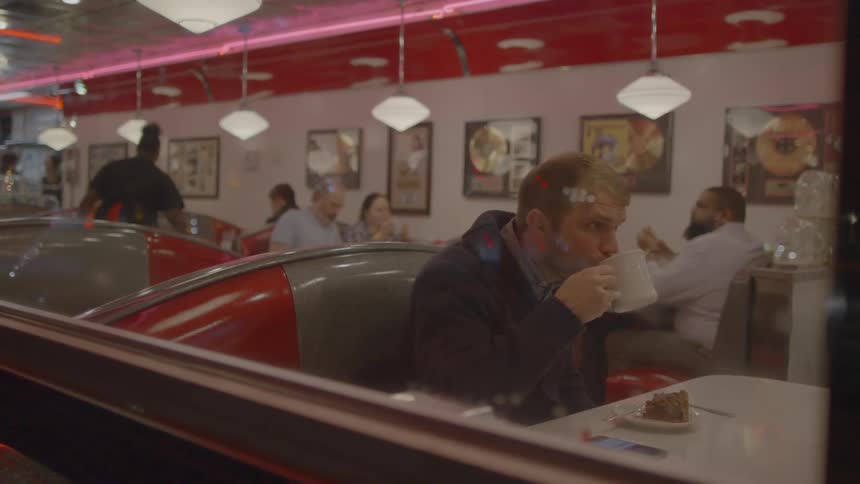 A man takes a drink from a mug in a diner