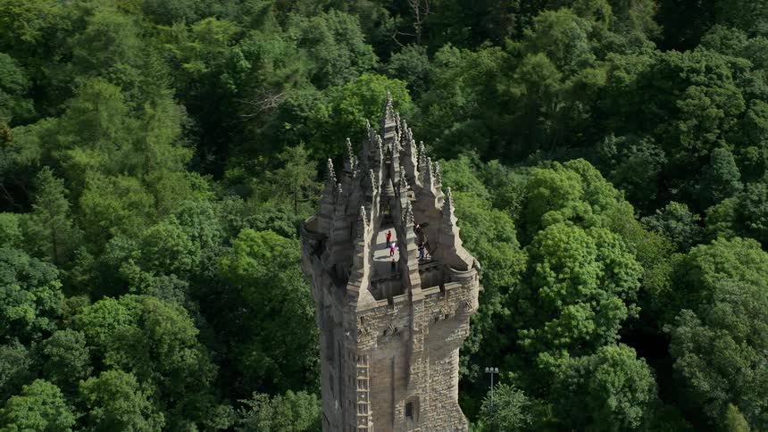 Aerial of a tower block surrounded by trees with people standing on its roof on a sunny day