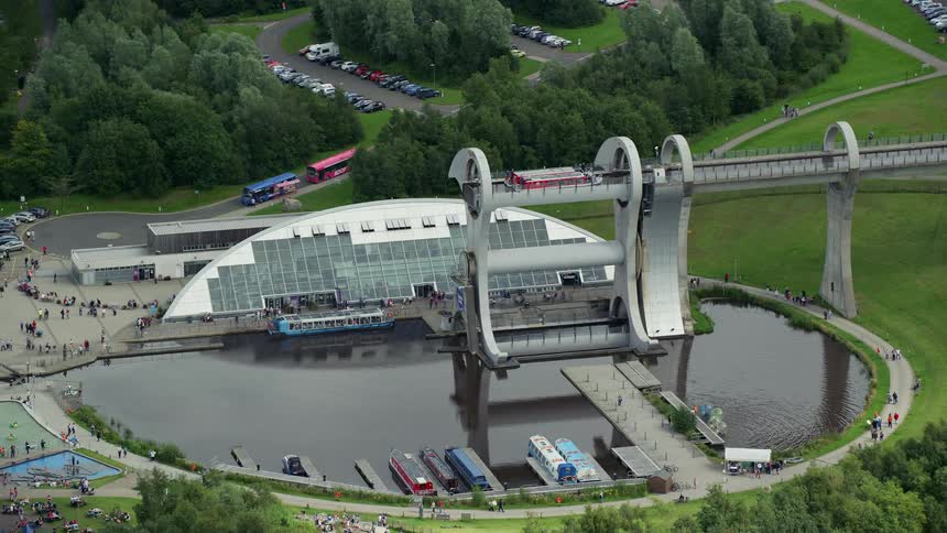Aerial view of a public area with a central lake a bridge and people walking around